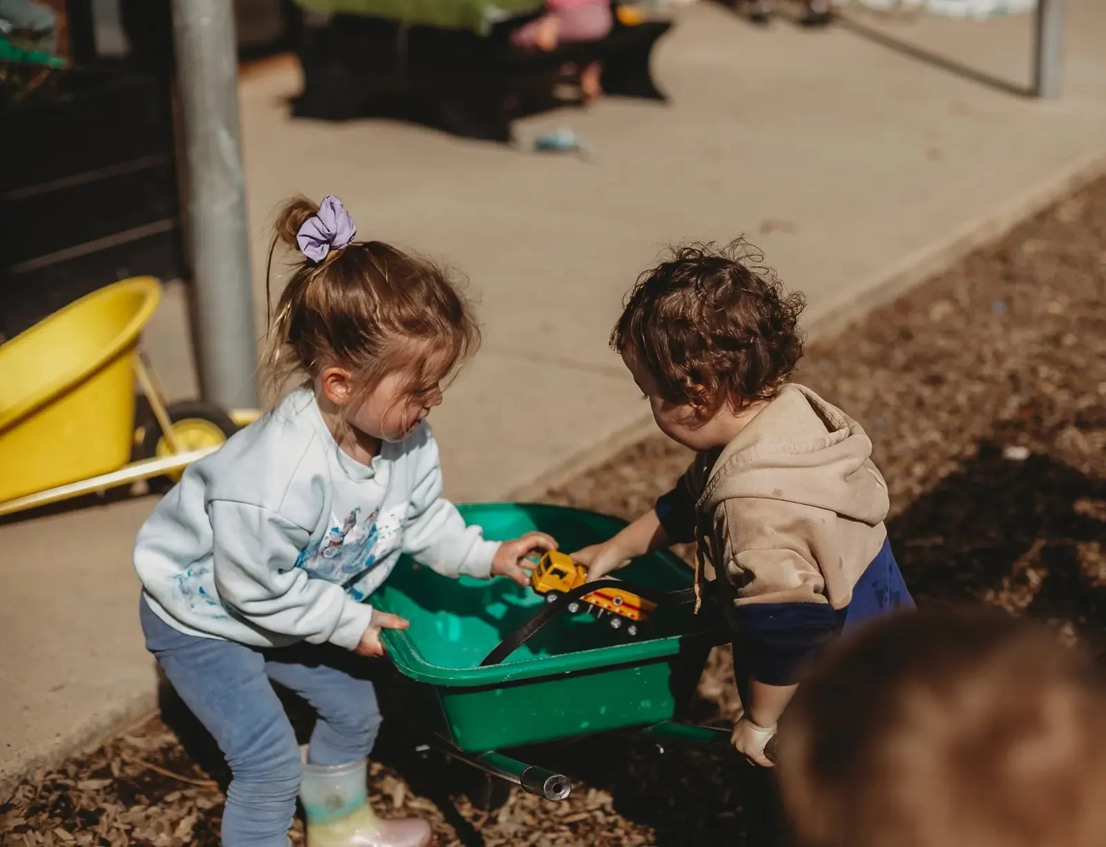 Children working together with a green wheelbarrow